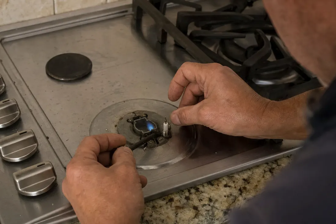 Hands relighting the igniter on a gas cooktop, one burner cap set aside, the stone countertop in frame - Wolf Repair Across the First Coast