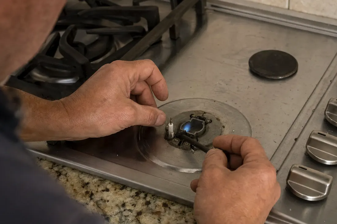 Hands relighting the igniter on a gas cooktop, one burner cap set aside, the burner grates in frame - Appliance Repair in Duval County