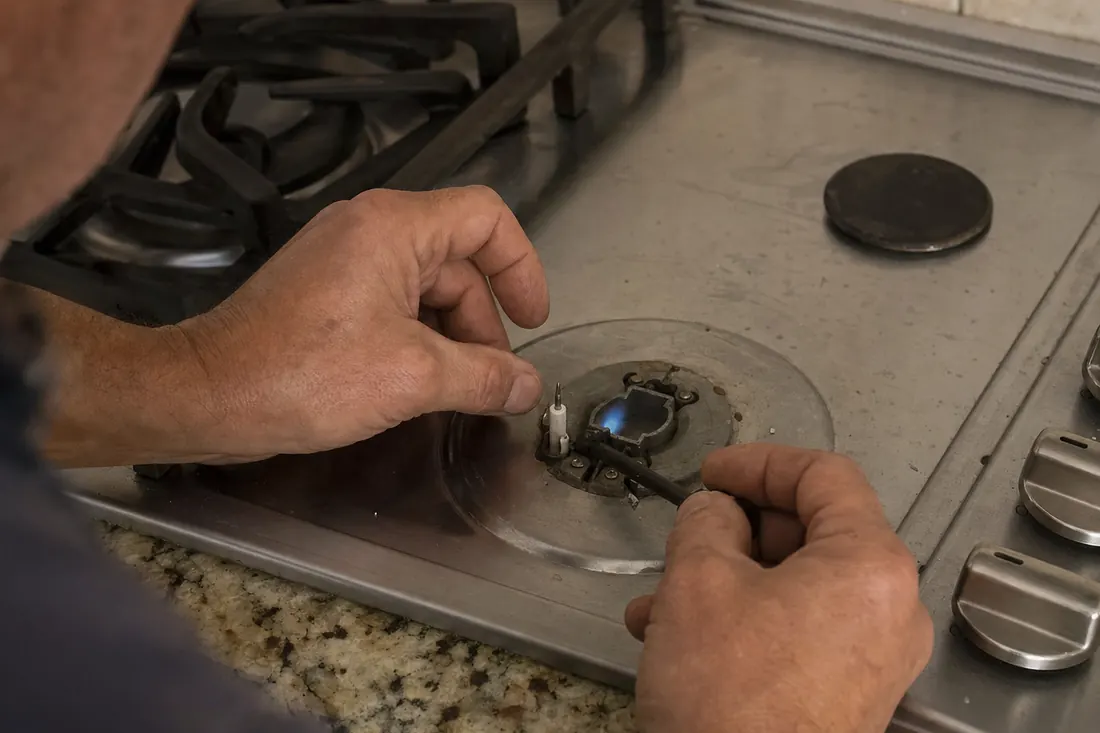 Hands relighting the igniter on a gas cooktop, one burner cap set aside, the removed burner cap visible in the picture - Pricing and the diagnostic visit