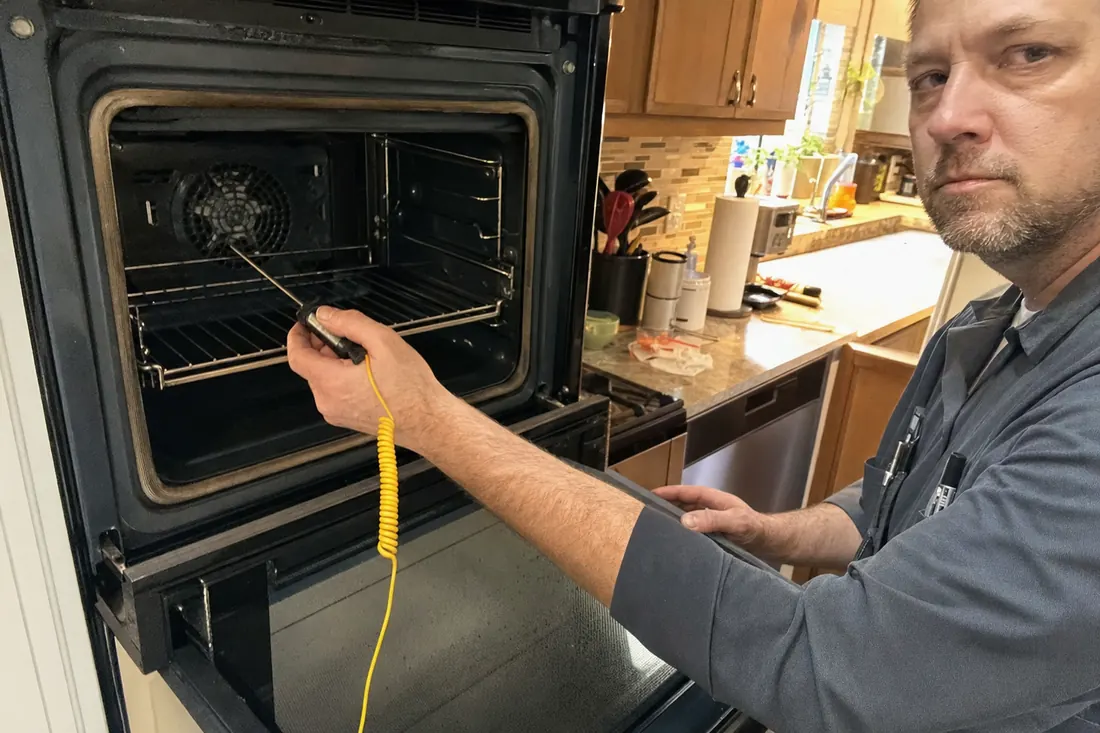 Technician holding a probe thermometer inside an open wall oven, the probe thermometer in frame - Browse by appliance type