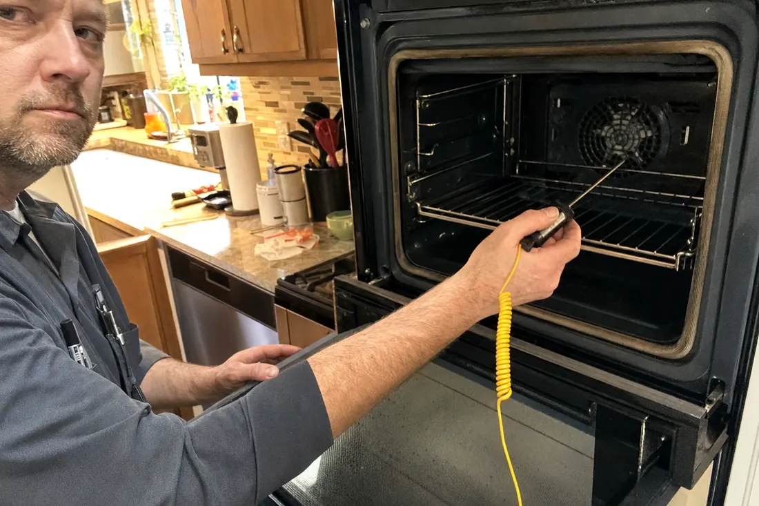 Technician holding a probe thermometer inside an open wall oven, the cavity walls in frame - Appliance Repair in Clay County