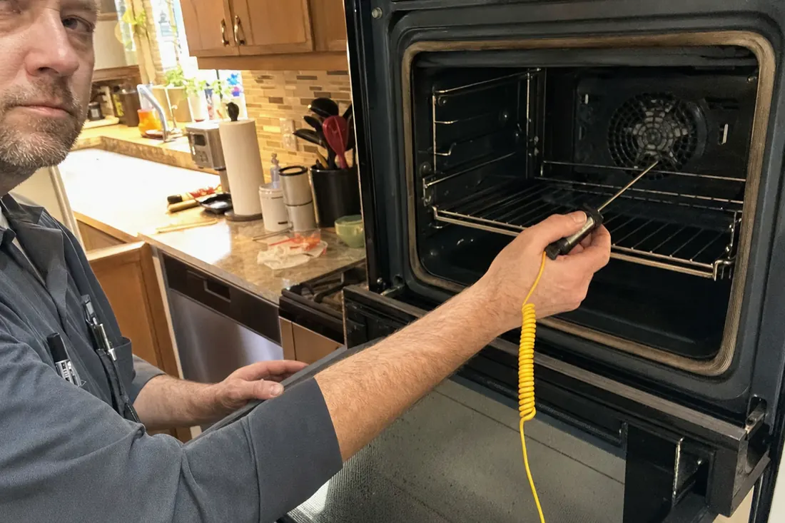 Technician holding a probe thermometer inside an open wall oven, the probe thermometer visible in the picture - Warranty on the work