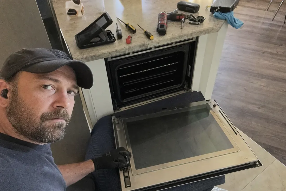 A wall oven door off its hinges on a moving blanket, hinge mechanism exposed - About First Coast Appliance Group