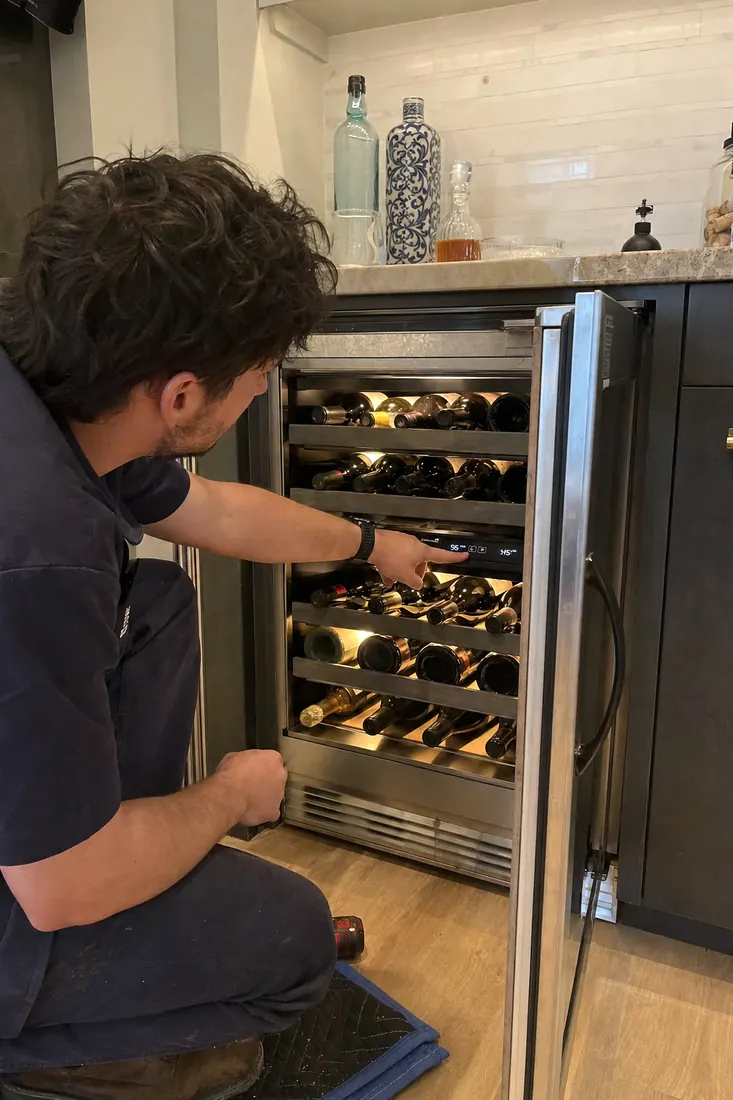 Technician at an open dual-zone wine unit, checking the temperature panel, bottles on the racks in frame - What to Check Before You Book a Service Visit